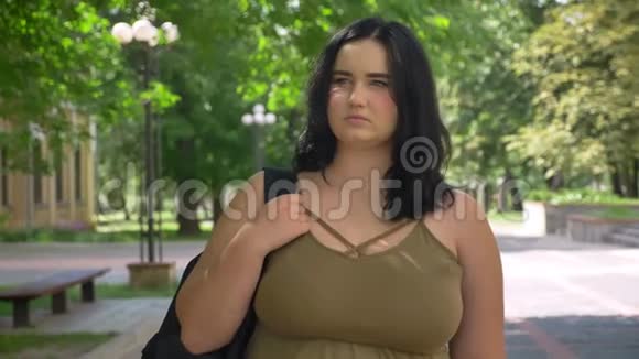 在阳光明媚的日子里一个肥胖的年轻女子在公园里四处张望站在街上视频的预览图