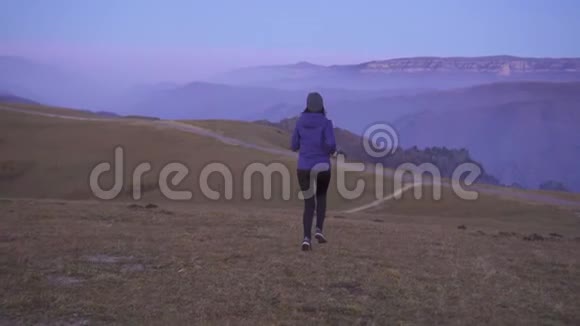 女运动员戴着帽子在背景山上奔跑从背后看慢悠悠地视频的预览图