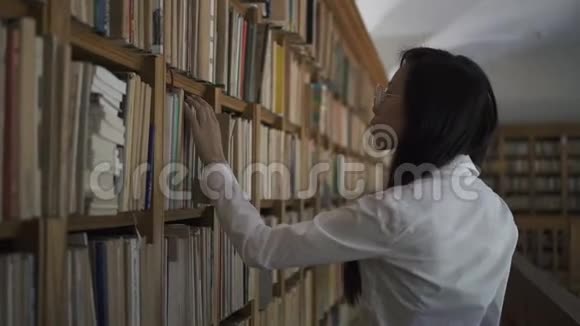 年轻的亚洲生物学家穿着白色衬衫的学生从书架上取旧书视频的预览图