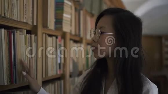 美丽的亚洲生物学家学生正在室内图书馆沿着书架行走视频的预览图