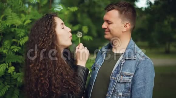 可爱夫妻在森林里嬉戏的慢动作女孩在男人脸上吹蒲公英视频的预览图