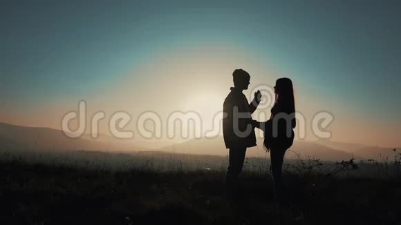 一对在山里相爱的夫妇的剪影徒步旅行者男人和女人站在山上手牵手视频的预览图