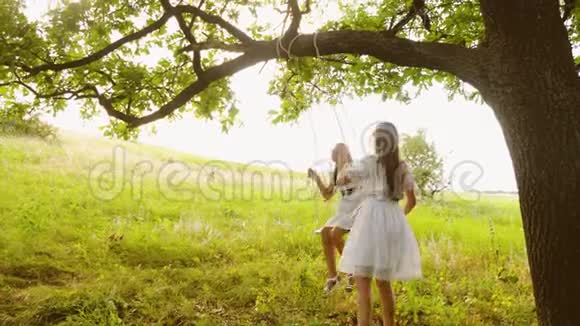 女朋友在一棵夏天的橡树下荡秋千笑了起来女孩青少年一起玩在大自然和微笑视频的预览图
