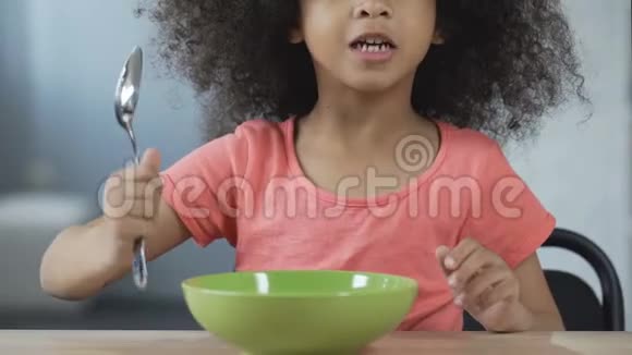 一个美国黑人小女孩拿着勺子坐在桌旁要求吃饭视频的预览图