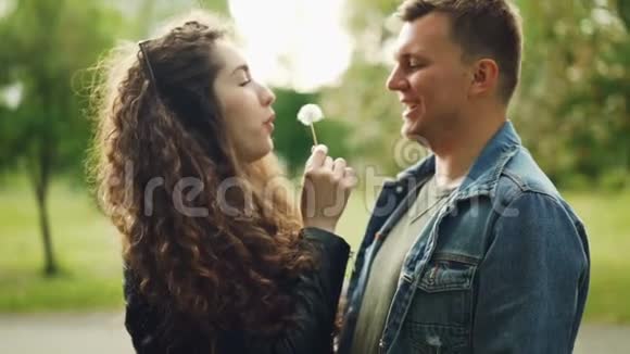 这对可爱的情侣在公园里玩得很开心年轻的女人正在男朋友脸上吹蒲公英吹球视频的预览图