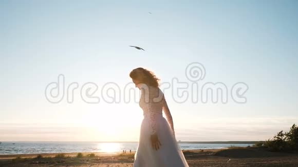 夏天年轻的新娘在海边跳跃在日落时分穿着婚纱的欧洲女人跳起来慢动作视频的预览图