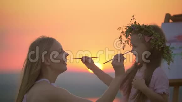 美丽的母亲和女儿在美丽的夕阳下用画笔在他们的有趣的绘画视频的预览图
