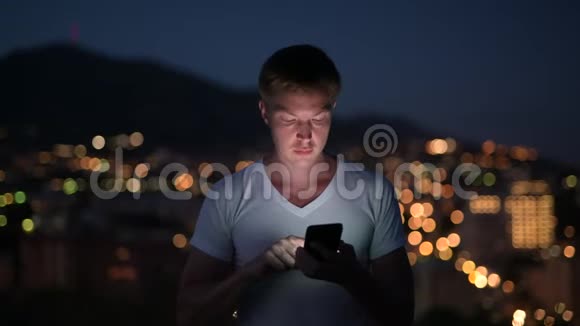 年轻快乐的游客晚上用电话看城市的灯光视频的预览图
