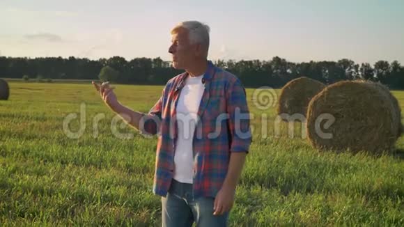 老农人站在草田上用手指着自己的土地傍晚的背景是美丽的大自然视频的预览图