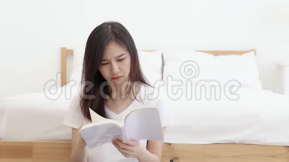 美丽的肖像年轻的亚洲女人坐着看书在家里的卧室里严肃认真视频的预览图