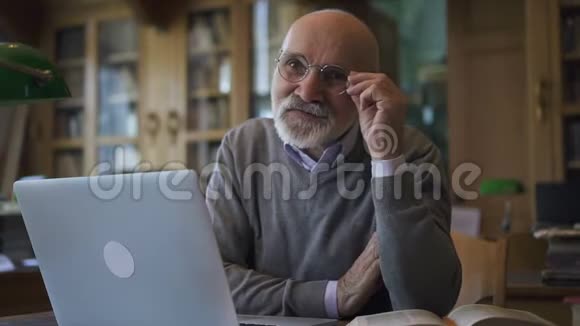 大学图书馆里的男性生物学家教授正在摆姿势坐在桌旁手提电脑视频的预览图