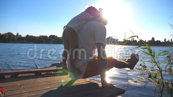 年轻人在湖边的木制码头边背着儿子练习瑜伽家庭花费时间视频的预览图