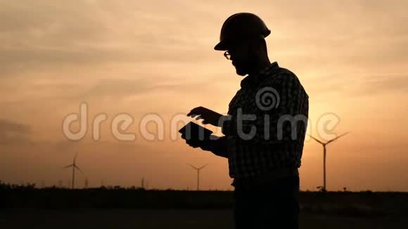 一位风力发电厂工程师的剪影手中拿着一块平板电脑背景是日落视频的预览图