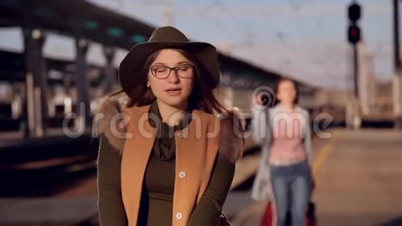 戴着眼镜和帽子的女孩在火车站等火车后面有个女孩问视频的预览图