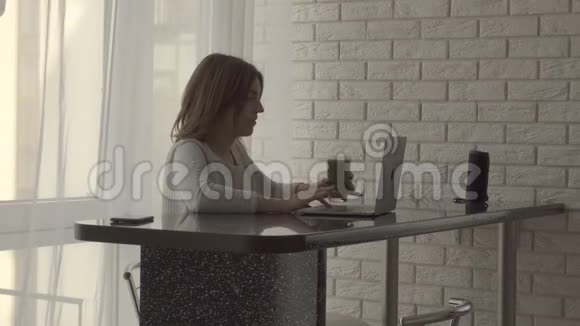 在家工作的女人坐在桌子旁喝着一大杯健康的绿色冰沙视频的预览图
