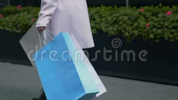 手里拿着纸袋的女士走在大街上走在商场正面绿色花坛的背景下视频的预览图