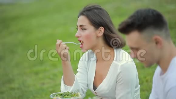 年轻夫妇坐在草地上吃沙拉一起野餐视频的预览图