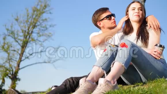 浪漫的夫妻喝咖啡笑着坐在池塘附近的绿草上夫妻信任爱情和幸福的概念视频的预览图