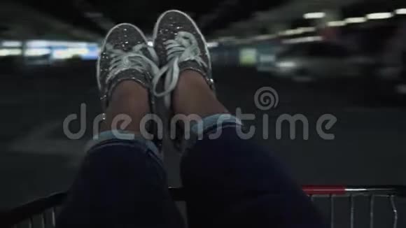 穿着银色闪亮运动鞋在停车场的购物车里盘旋的女足视频的预览图