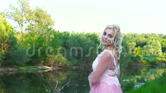 夏天日落时一个穿着粉红色连衣裙的漂亮女孩在河边化妆的肖像视频的预览图