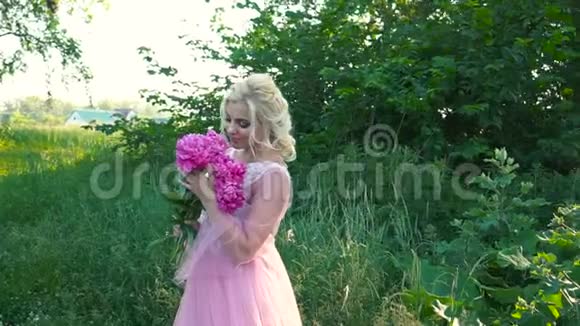 年轻的金发女人穿着粉红色的裙子拿着一束花在镜头前摆姿势视频的预览图