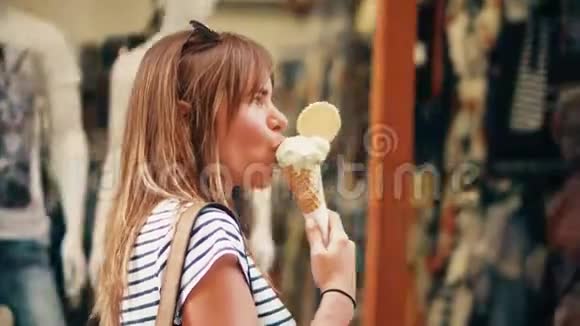 美丽的年轻女子吃着冰淇淋筒走在街上视频的预览图