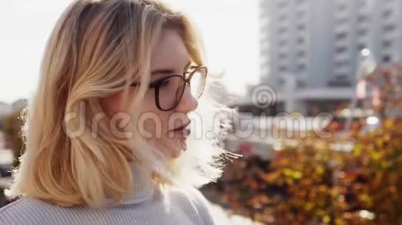 美丽的金发女郎戴着眼镜望着阳光明媚的秋天城市视频的预览图