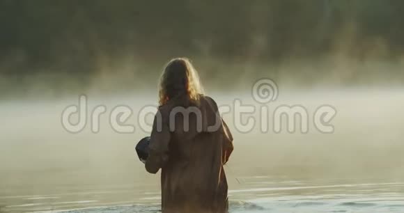 小女孩拿着一个盒子走在湖里她在旁边拖着一把刀在自然的绿色视野中慢慢地视频的预览图