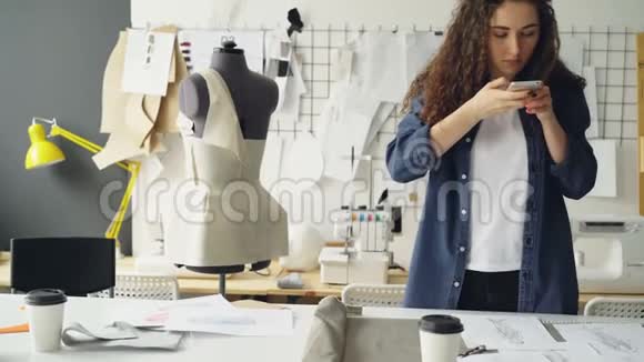 服装设计师enterreneur正用智能手机在工作室办公桌上拍摄平面服装草图和咖啡视频的预览图