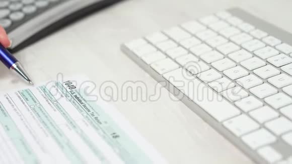 在电脑键盘和键盘旁边的桌子上人手通过1040税单后的特写滑块运动视频的预览图