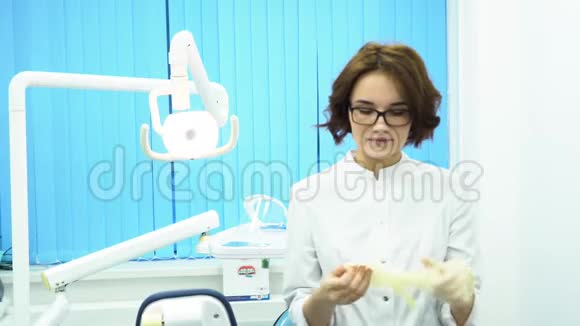 年轻的女医生戴着眼镜和一件白色的外套在牙科诊所的戴上白色的医疗手套严格的视频的预览图