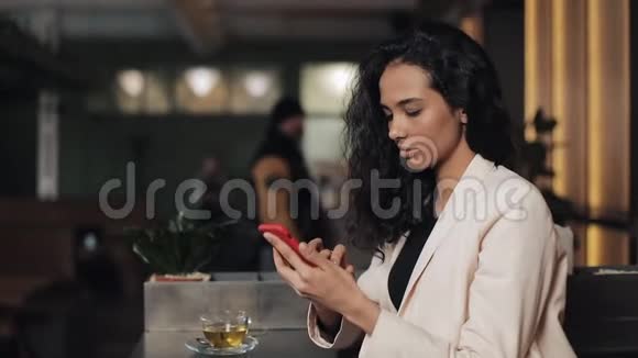 漂亮的年轻女商人在舒适的咖啡馆里使用智能手机女孩微笑着在网上和朋友聊天视频的预览图