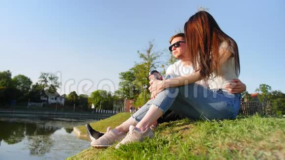 浪漫的夫妻喝咖啡笑着坐在池塘附近的绿草上夫妻信任爱情和幸福的概念视频的预览图