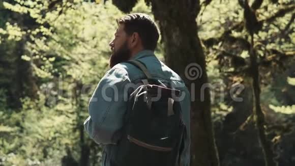 长胡子的人背着背包站在一个平坦的国家看着树视频的预览图