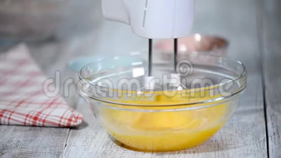 厨师用手搅拌器在碗里打鸡蛋做蛋糕蛋糕配料在桌子上视频的预览图