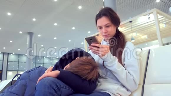 女人带着疲惫的儿子在机场大厅的手机上在线登记视频的预览图