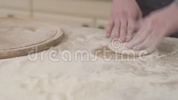 在家里用面团擀面杖准备面团用围裙把年轻的披萨制造商的手收起来食物概念视频的预览图