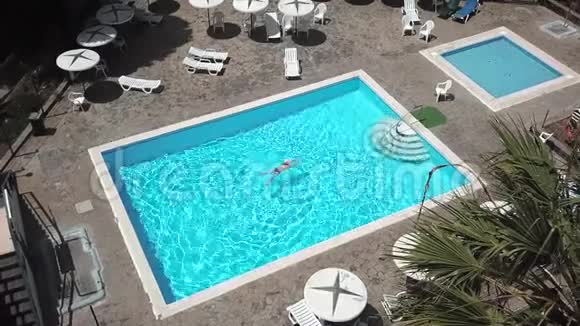 从顶部看穿着蓝色泳衣的女人在酒店别墅或公寓的游泳池游泳视频的预览图