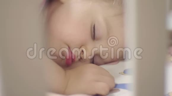 两岁的小女孩睡在铺着白色毯子的婴儿床上日间睡眠视频的预览图