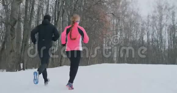 年轻的一家人在冬天的森林里晨跑穿宽松夹克的女人穿黑衣的男人视频的预览图