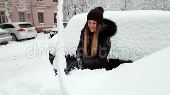 早上暴风雪过后微笑的女司机把雪从车上移走视频的预览图