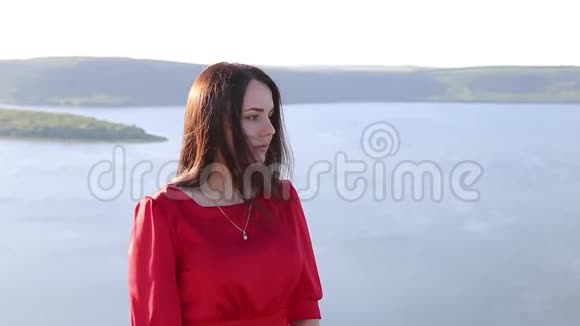 美丽的欧洲女人穿着红色的衣服在大河岸边看着令人惊叹的背景巨大的河流日落视频的预览图
