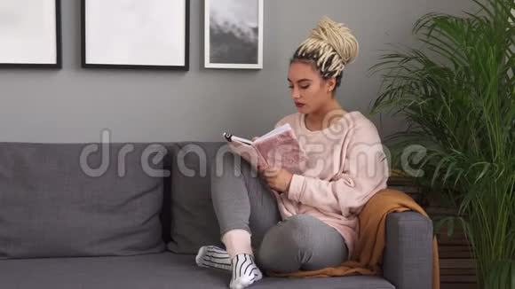 年轻女性坐在舒适的沙发上写着笔记本视频的预览图