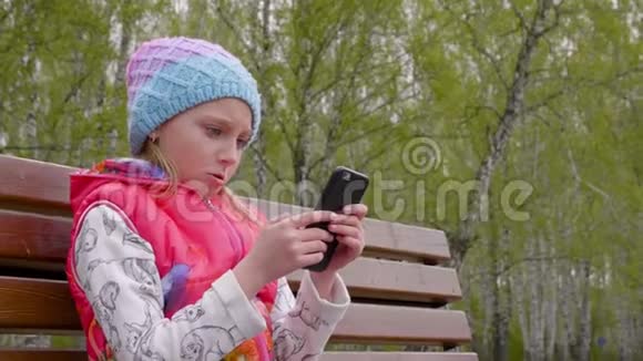 兴奋的少女坐在公园的长凳上用电话视频的预览图