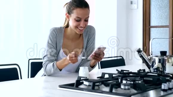 漂亮的年轻女人在家吃酸奶的时候用手机发信息视频的预览图