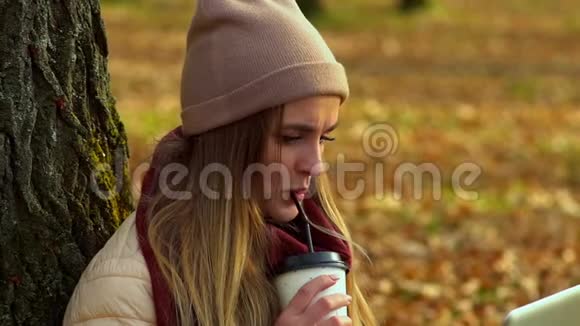 美丽的女孩秋天在公园里喝着咖啡看着笔记本电脑的屏幕视频的预览图
