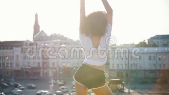 迷人的莫拉托年轻女子卷发在现代建筑的背景下跳舞日落视频的预览图