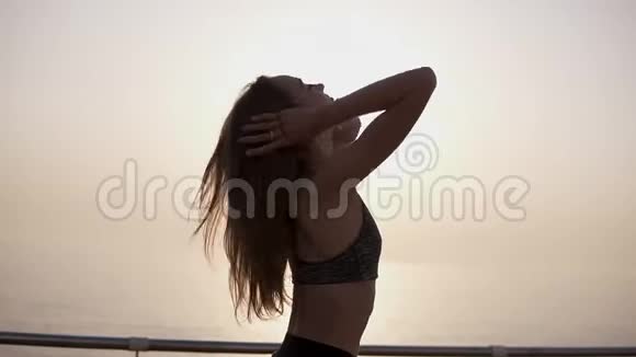 一个穿着运动胸罩的漂亮女孩站在海景前阳光明媚把她的长发梳成视频的预览图