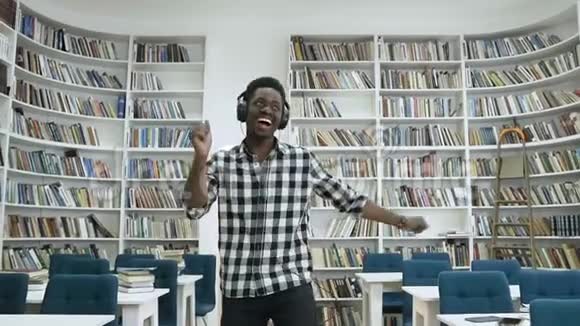 快乐的非洲男人在耳机里听音乐在现代图书馆跳舞视频的预览图
