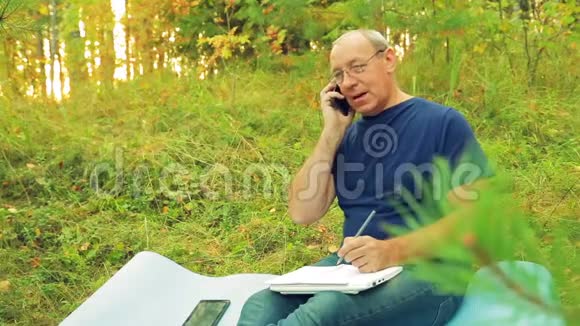 森林里的一个人在笔记本上写字在手机上说话视频的预览图